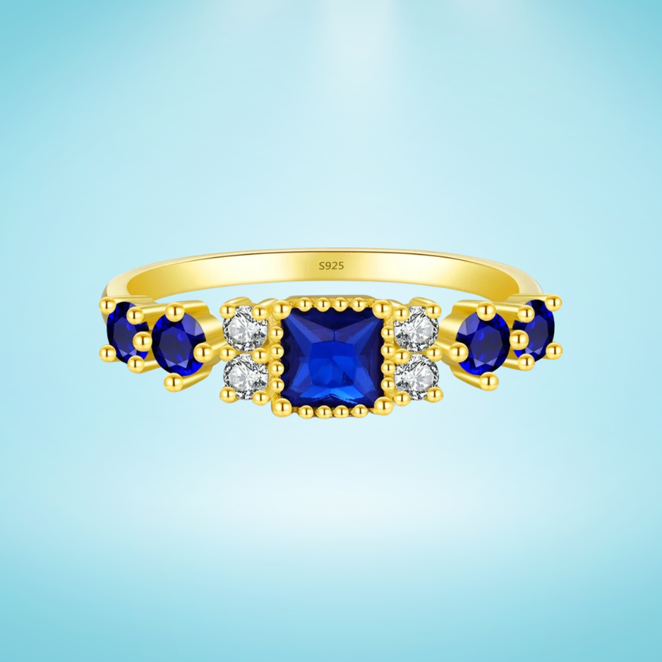 Gold-plated sterling silver ring with a central square-cut deep blue stone and surrounding clear round stones