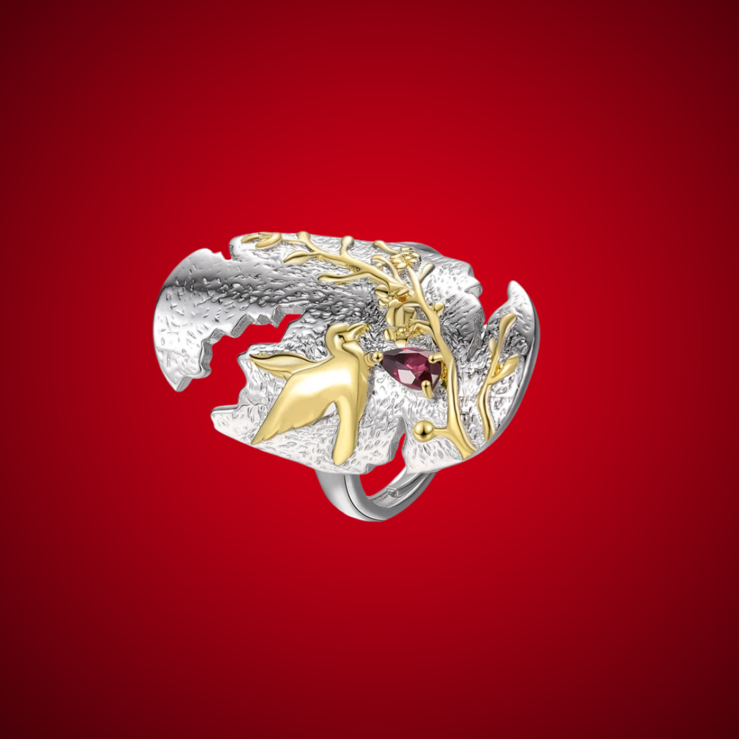 Sculpted silver ring featuring a golden hummingbird and branch detail with a red teardrop gemstone.