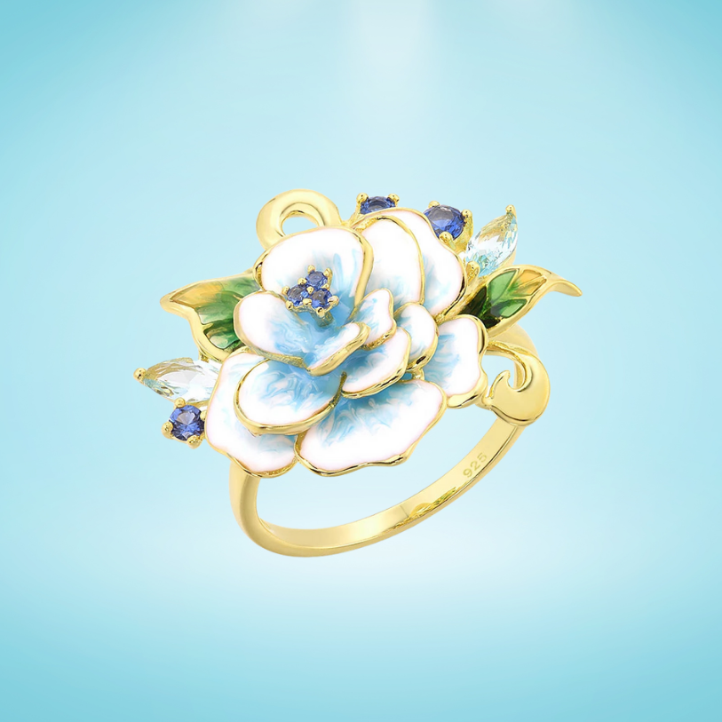 Gold-plated ring featuring a hand-painted white and blue enamel flower with gemstone accents and green enamel leaves
