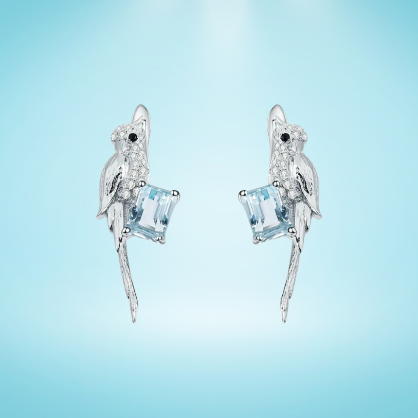 Silver earrings shaped like birds holding pale blue square-cut gemstones