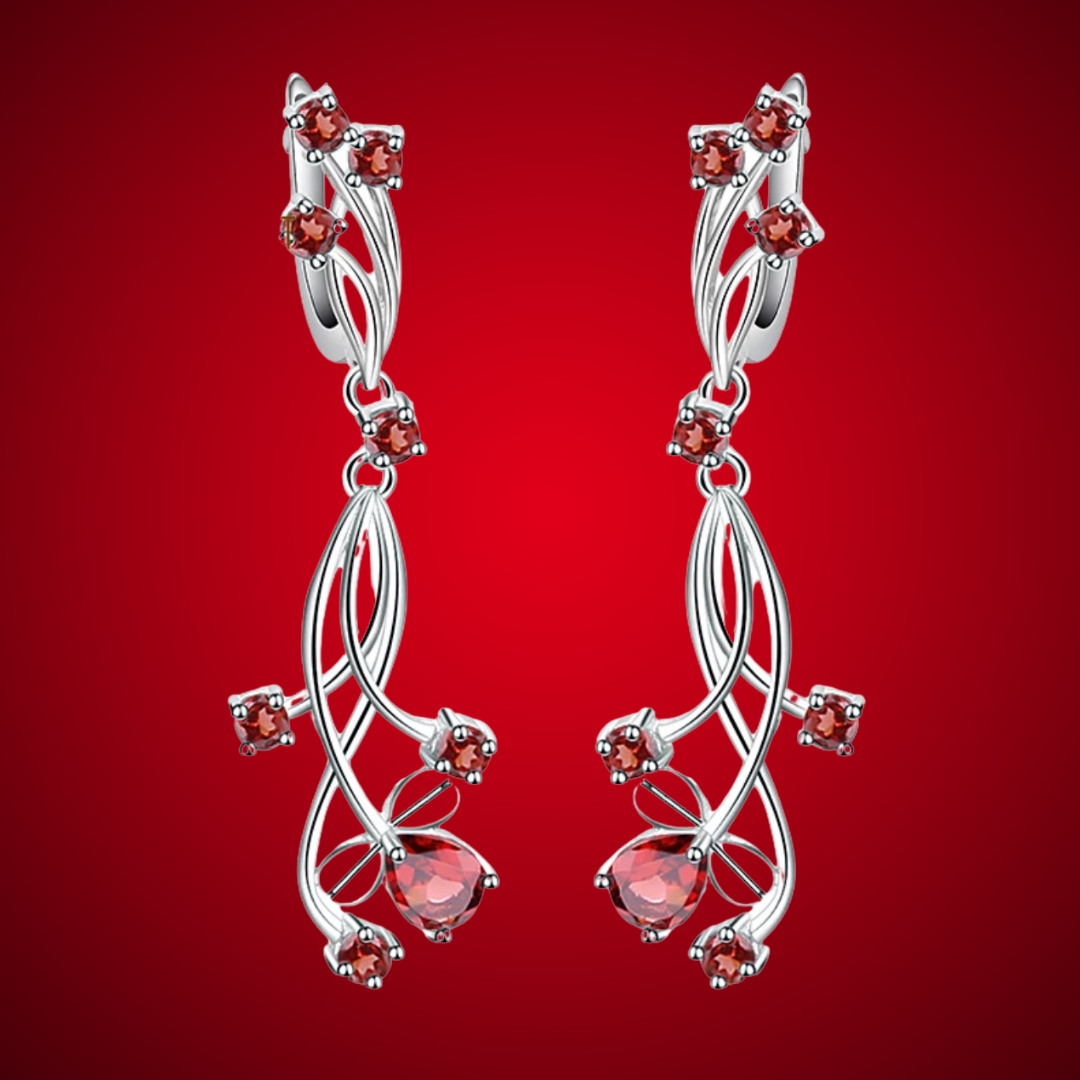Pair of silver drop earrings with delicate red gemstones, featuring interlaced curves and teardrop-shaped red stones.