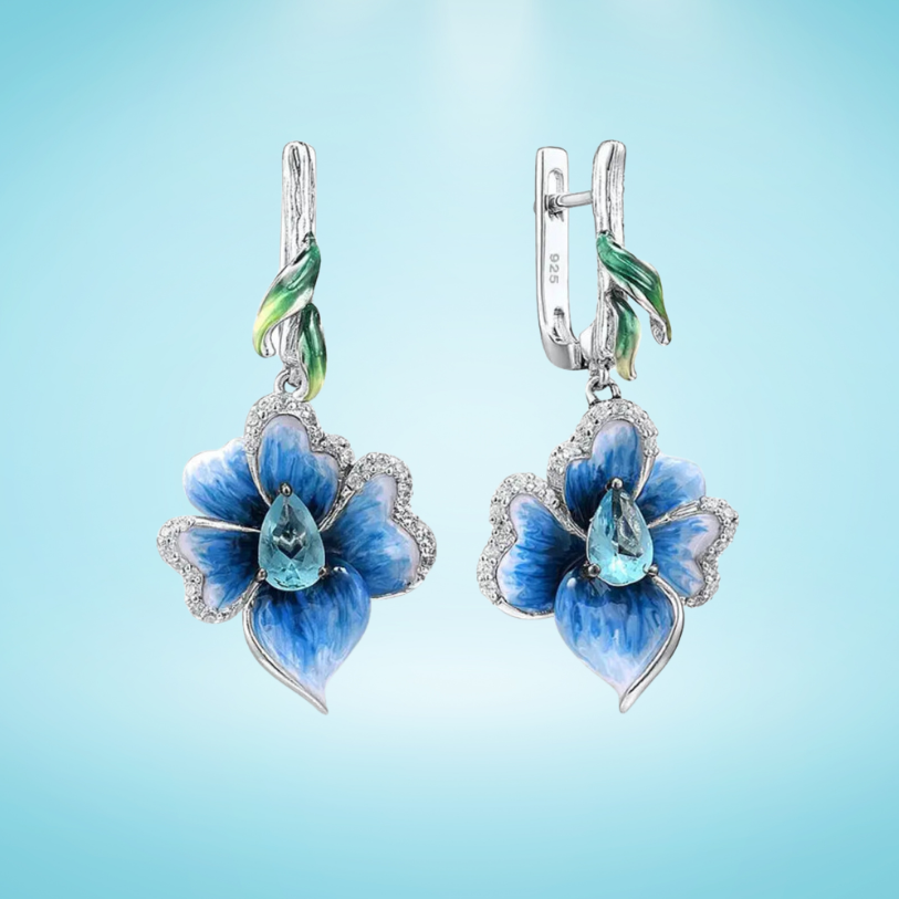 Silver floral earrings with hand-painted blue petals, green enamel accents, and teardrop blue stones.