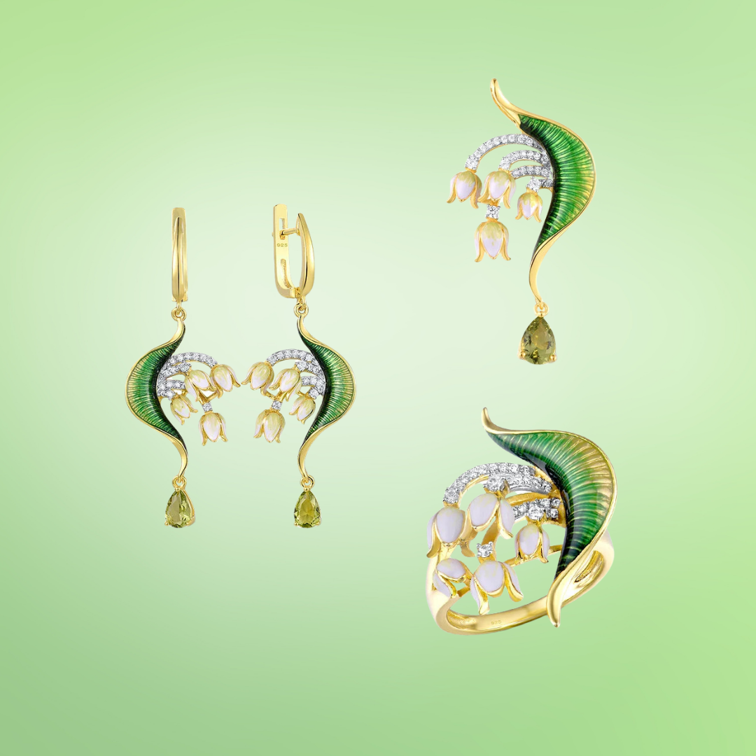 Close-up of a nature-inspired jewelry set featuring a green enameled leaf design with white and yellow floral elements, accented with sparkling stones and gold detailing.