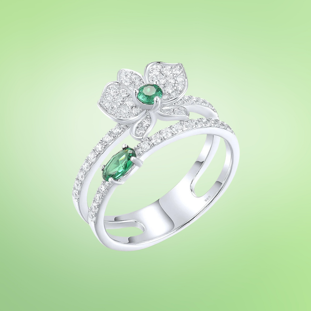 Silver ring featuring a sparkling orchid flower design with green and clear stones and a double-band setting