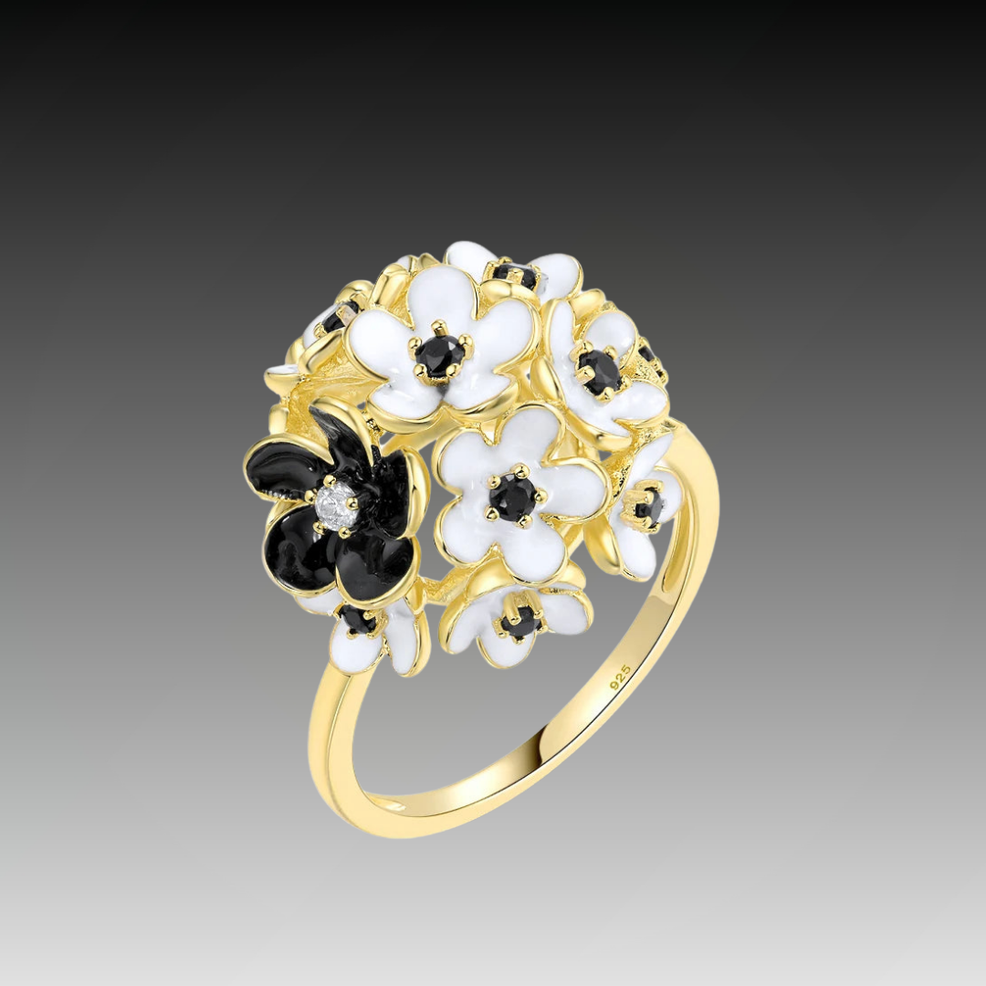 Gold ring featuring a cluster of white and black enamel flowers with dark gemstone centers.