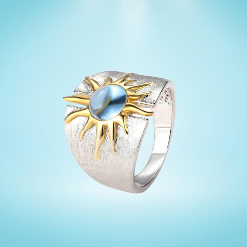 Silver ring with a textured band, featuring a golden sun design and a glossy blue stone at the center