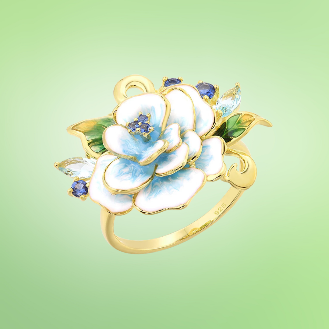 Gold ring with layered white and blue flower, green leaves, and blue gemstone accents