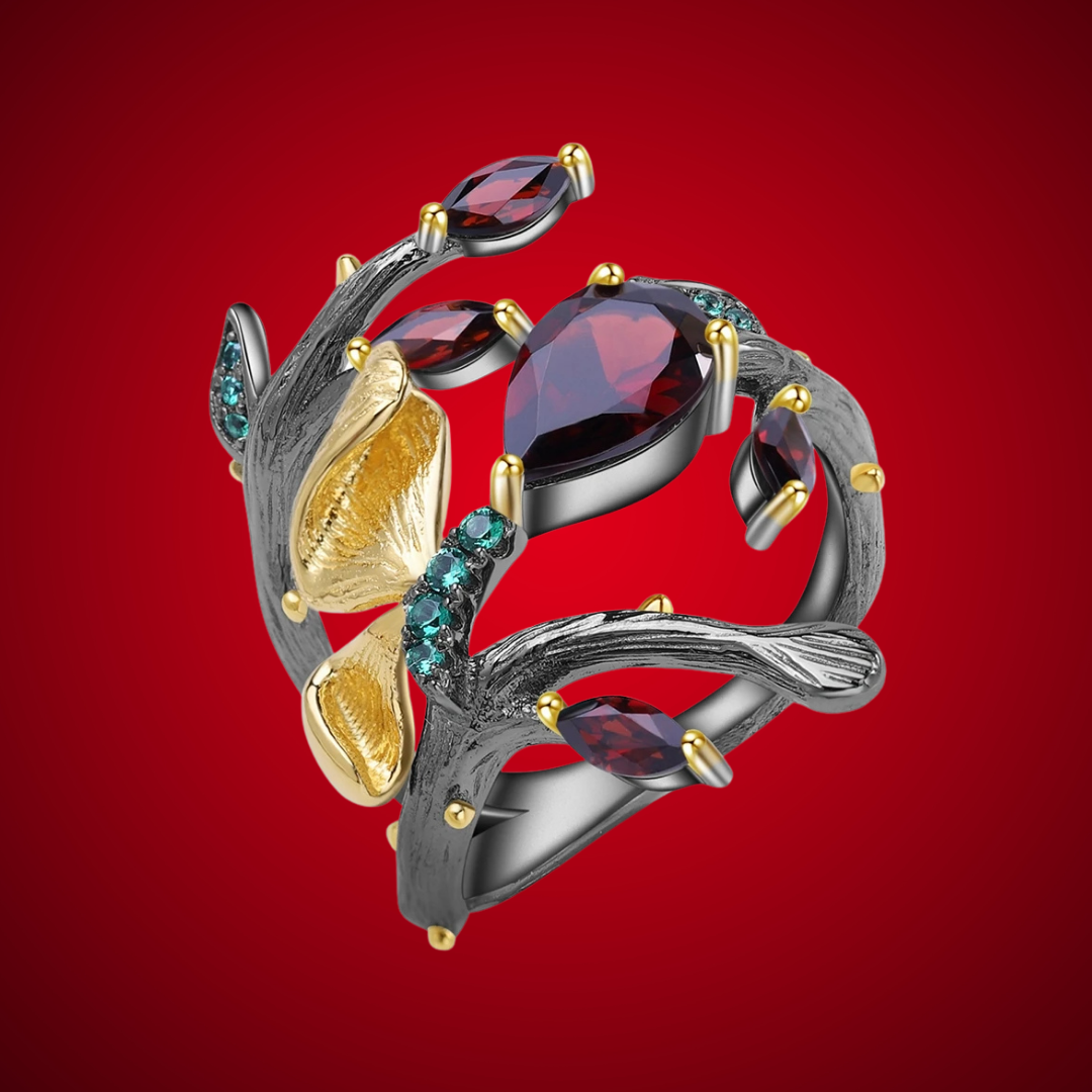 Dark branch-like ring with red marquise and teardrop stones, accented by gold floral elements and small green gems.