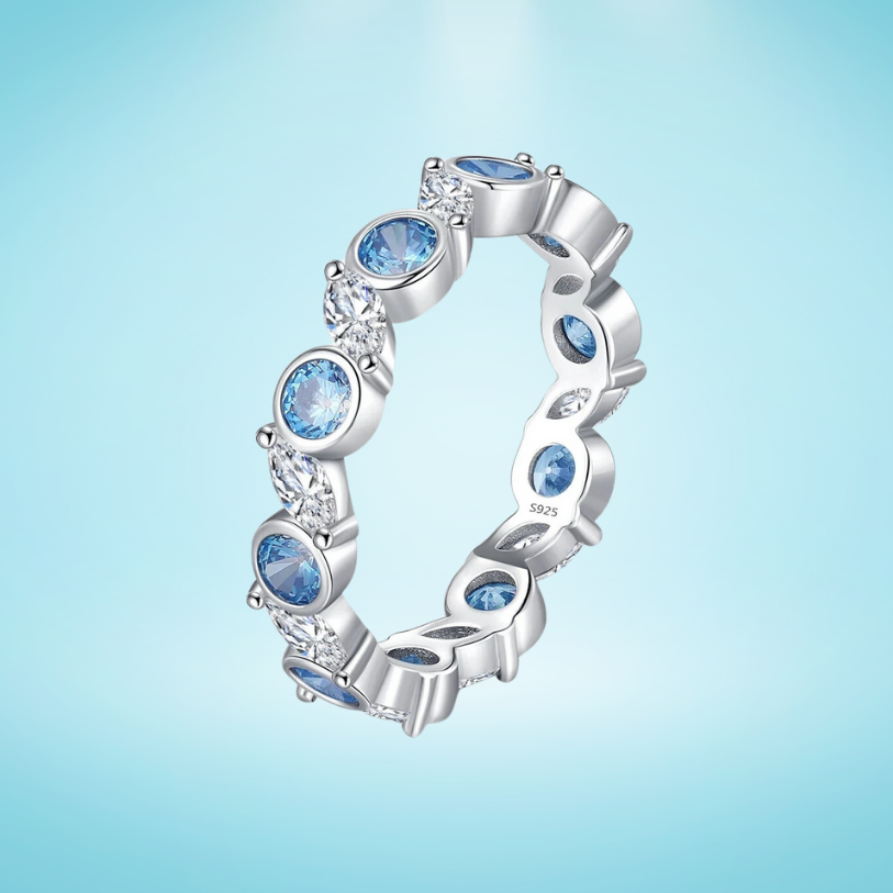 Sterling silver eternity ring with alternating light blue and clear round stones in bezel and prong settings
