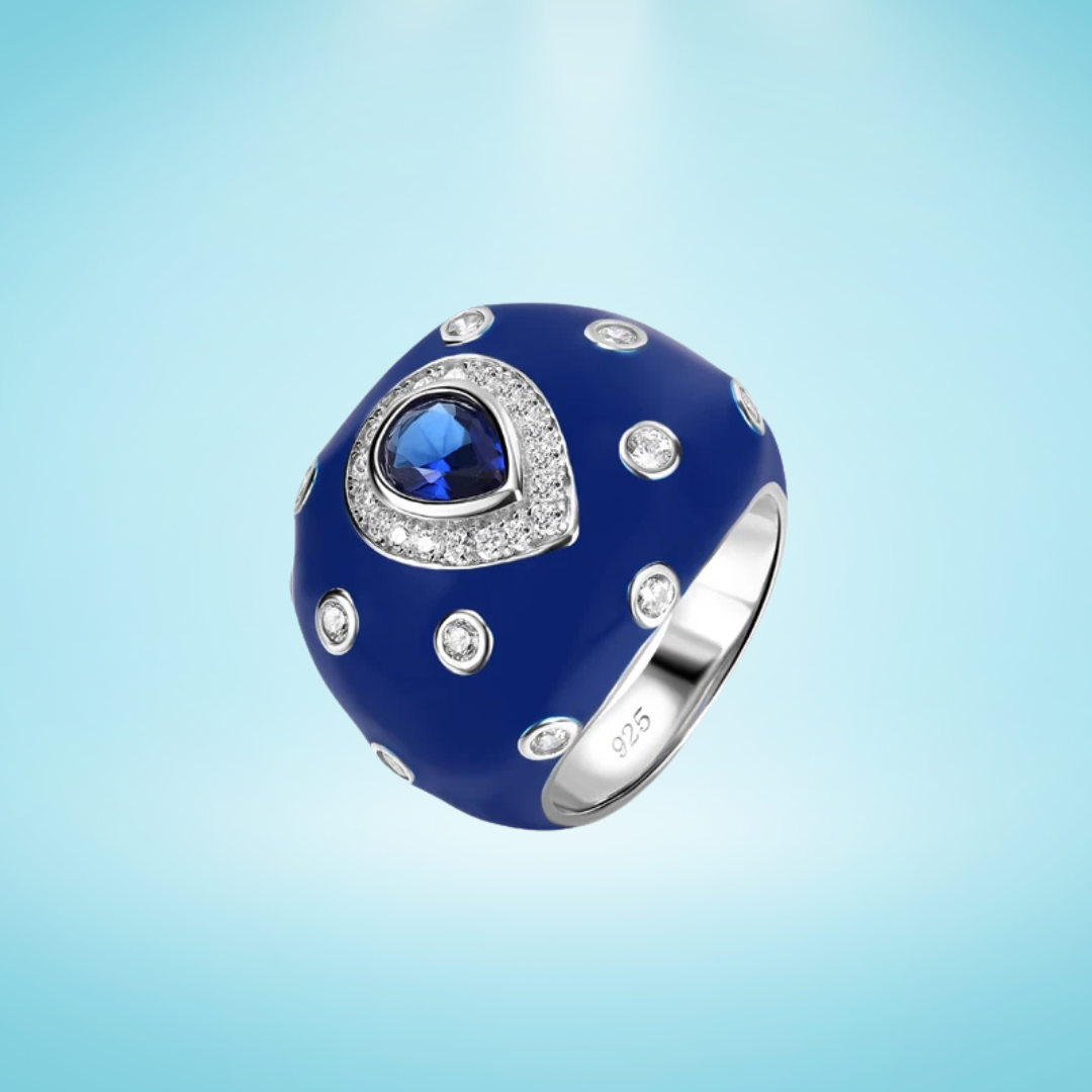 Sterling silver ring with a domed cobalt blue enamel surface, featuring a central teardrop blue gemstone and scattered clear crystals, on a light blue background