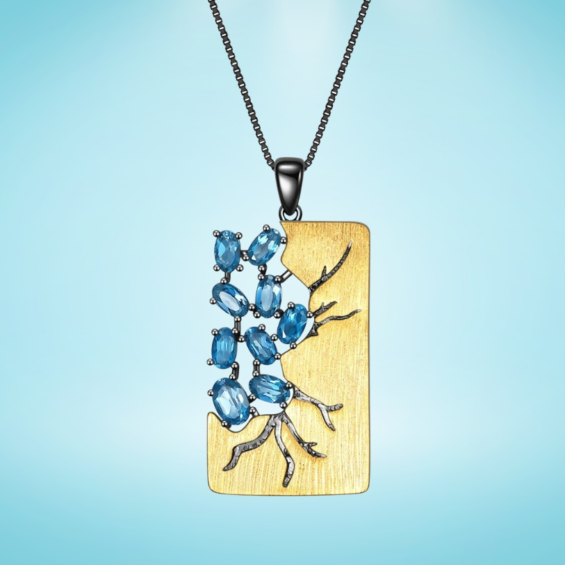 Rectangular gold pendant featuring dark branch-like details set with oval blue gemstones, hanging from a black chain