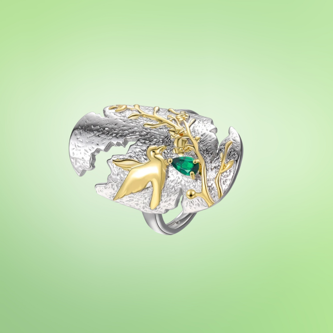 Silver and gold ring with a bird in flight and green gemstone on textured background