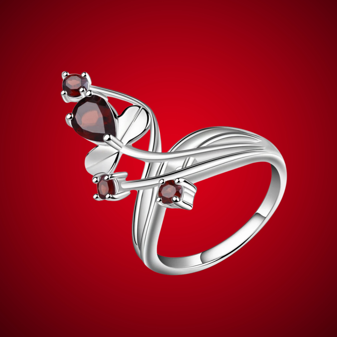 Silver ring with a curved, nature-inspired design, set with deep red round and pear-shaped stones.