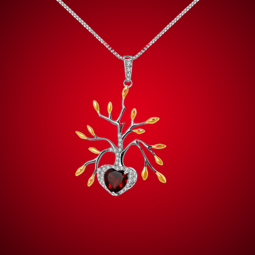 Pendant necklace featuring a tree-like silver structure with yellow leaf details and a heart-shaped red gemstone.