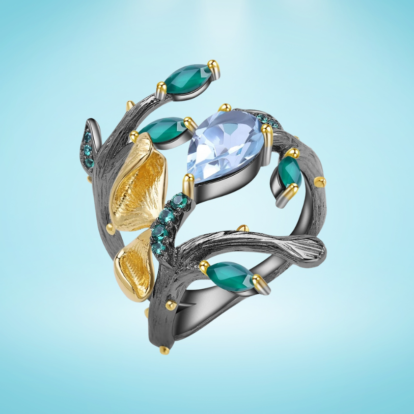 Black branch-style ring with sky-blue and green stones, gold leaves, and textured detailing
