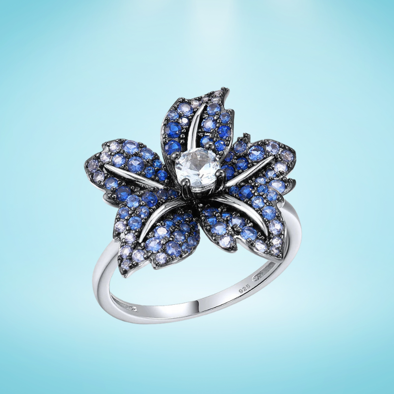 Silver ring shaped like a flower, with deep blue pavé stones and a clear central gem