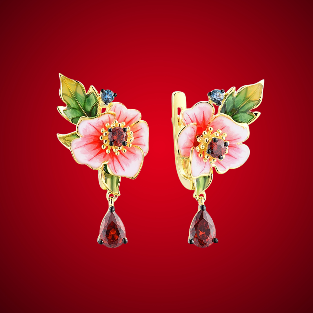 Gold earrings featuring pink enamel amaryllis flowers with green leaves and deep red teardrop stones, from the Rossa Collection.