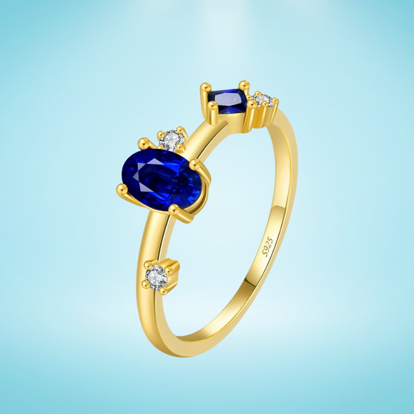 Gold-plated ring with deep blue oval and round stones set in a modern scattered design