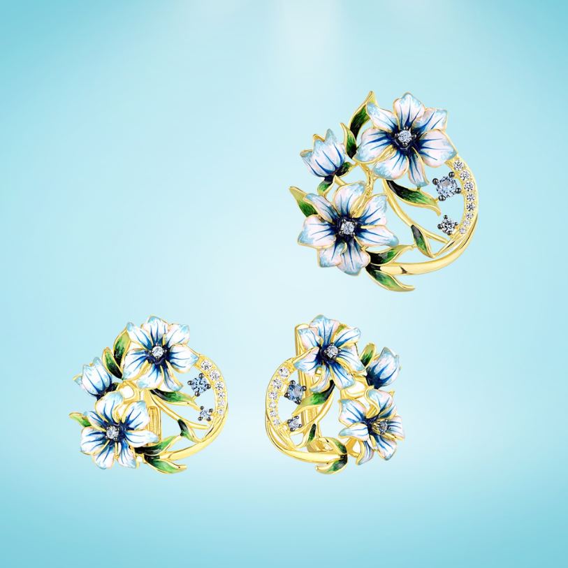 Gold floral jewelry set with white and blue enamel blossoms, green leaves, and delicate cubic zirconia curves