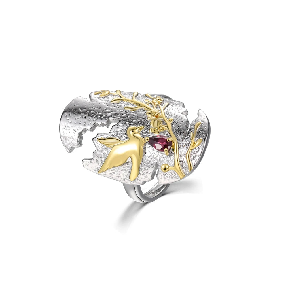 Sculpted silver ring featuring a golden hummingbird and branch detail with a red teardrop gemstone.