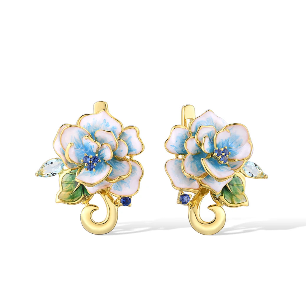 Gold-tone enamel earrings shaped like white and sky blue flowers with green leaves and sparkling stones.