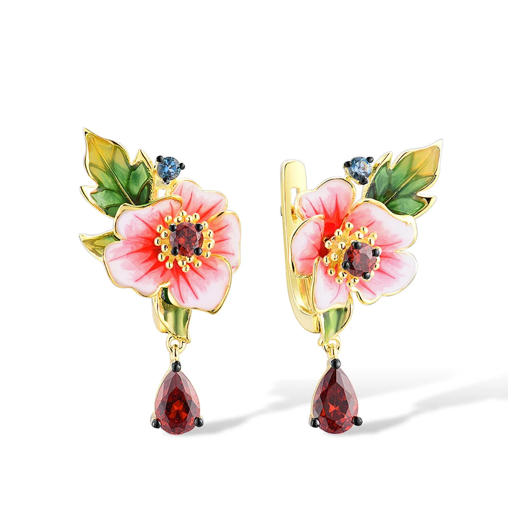 Gold earrings featuring pink enamel amaryllis flowers with green leaves and deep red teardrop stones, from the Rossa Collection.