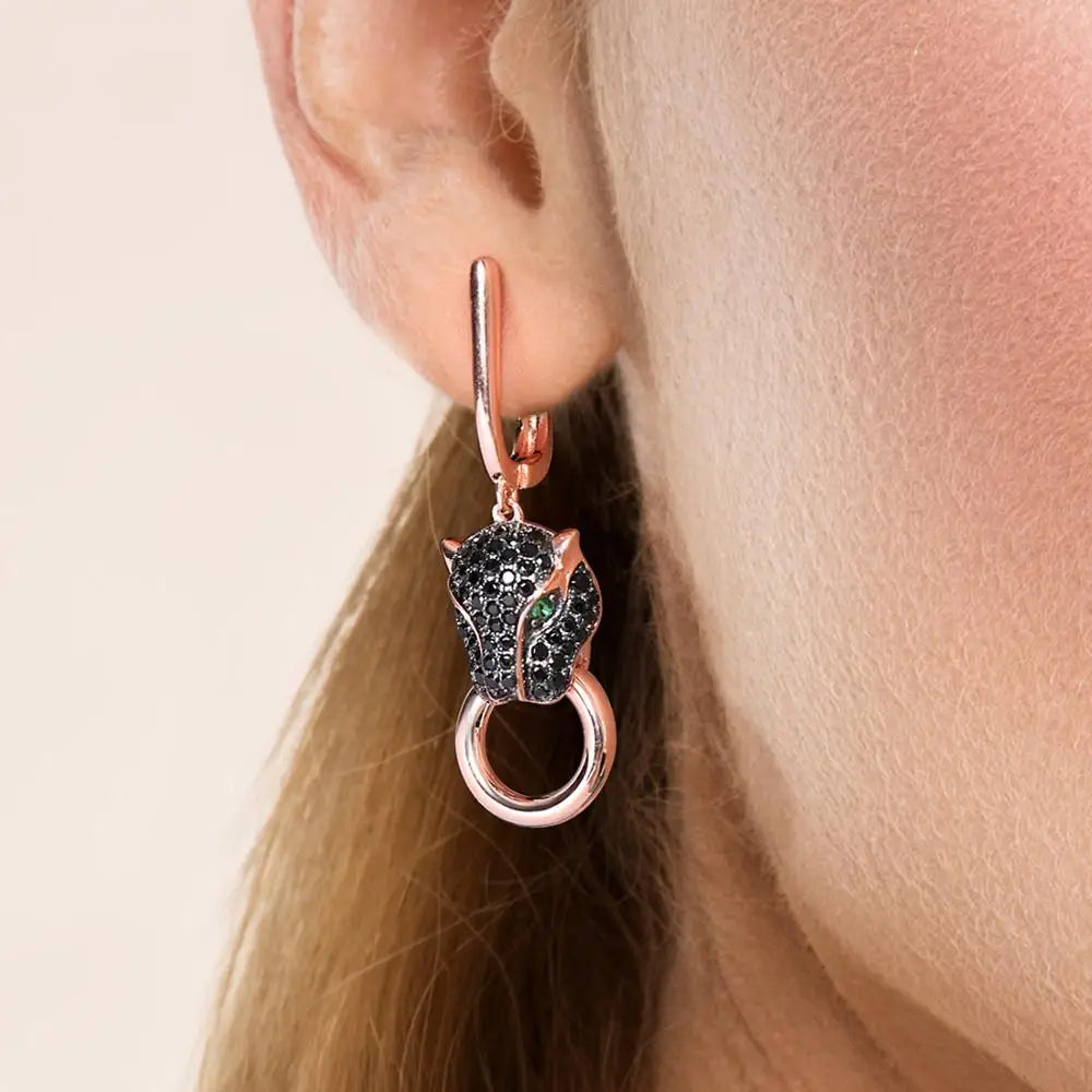 Rose gold earrings featuring black panther heads with green gemstone eyes and ring details.