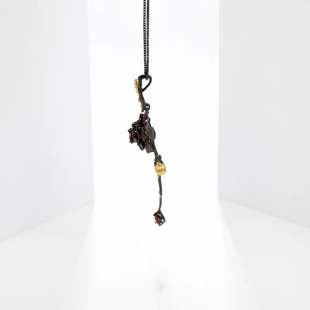 Pendant necklace with a dark rose-shaped bloom in ruby stones, accented by golden leaves and a delicate drop, from the Rossa Collection.
