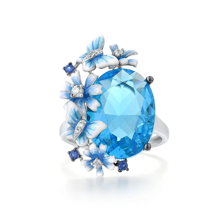 Silver ring with a large blue gemstone surrounded by butterflies and enamel flowers in soft blue tones