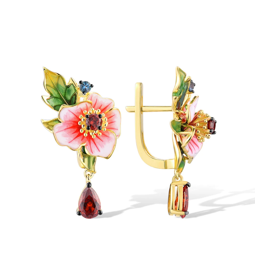 Gold earrings featuring pink enamel amaryllis flowers with green leaves and deep red teardrop stones, from the Rossa Collection.