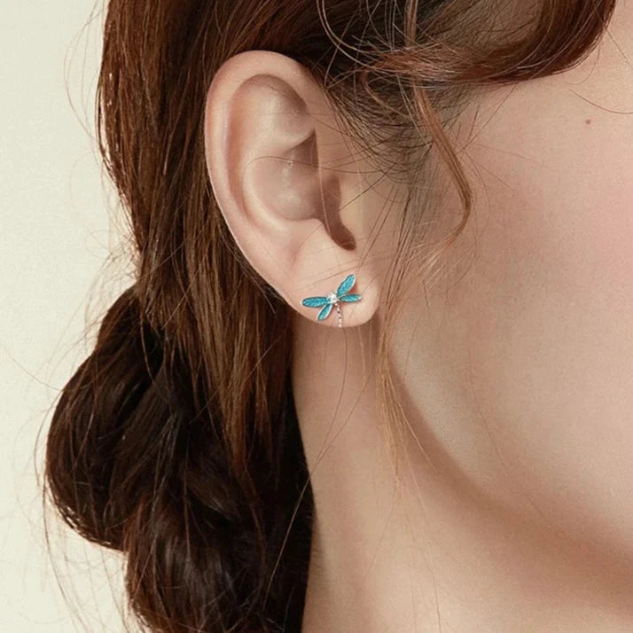 Silver dragonfly stud earrings with translucent blue enamel wings and a tiny clear gemstone on the body