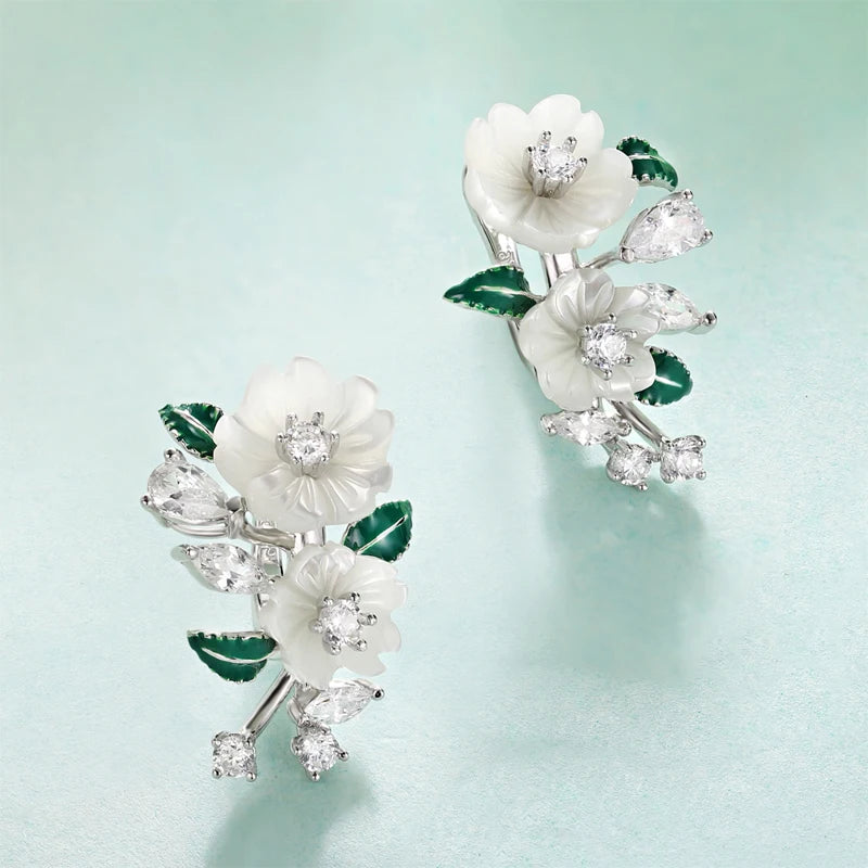 Silver earrings with carved white flowers, green enamel leaves, and clear gemstones