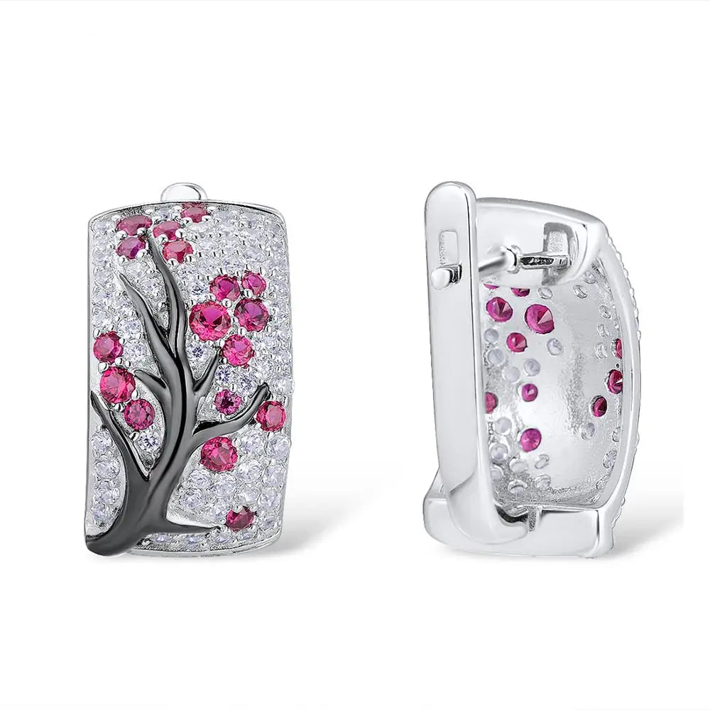Silver earrings featuring raised black branches with scattered red blossom-like stones.