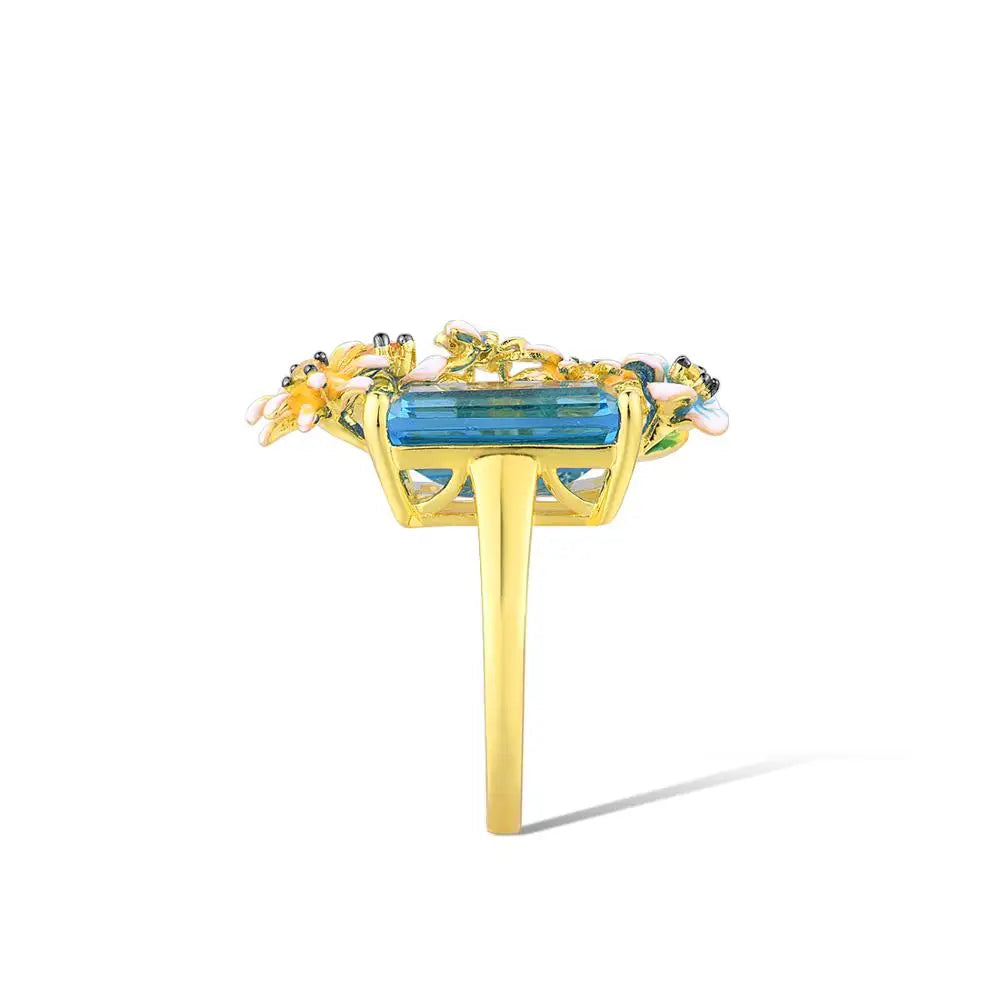 Gold ring with a large rectangular blue gemstone and colorful enamel flowers arranged around it