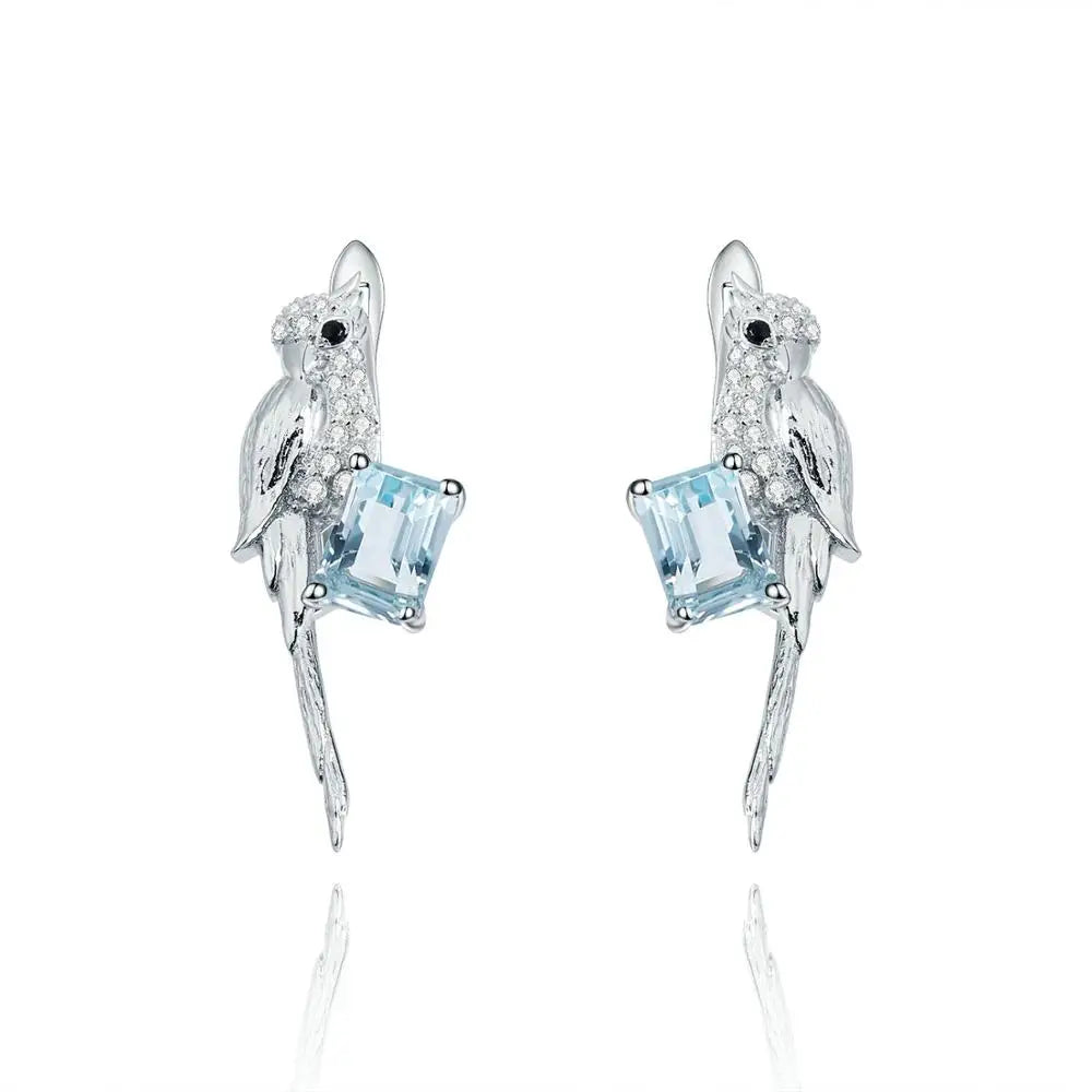 Silver earrings shaped like birds holding pale blue square-cut gemstones