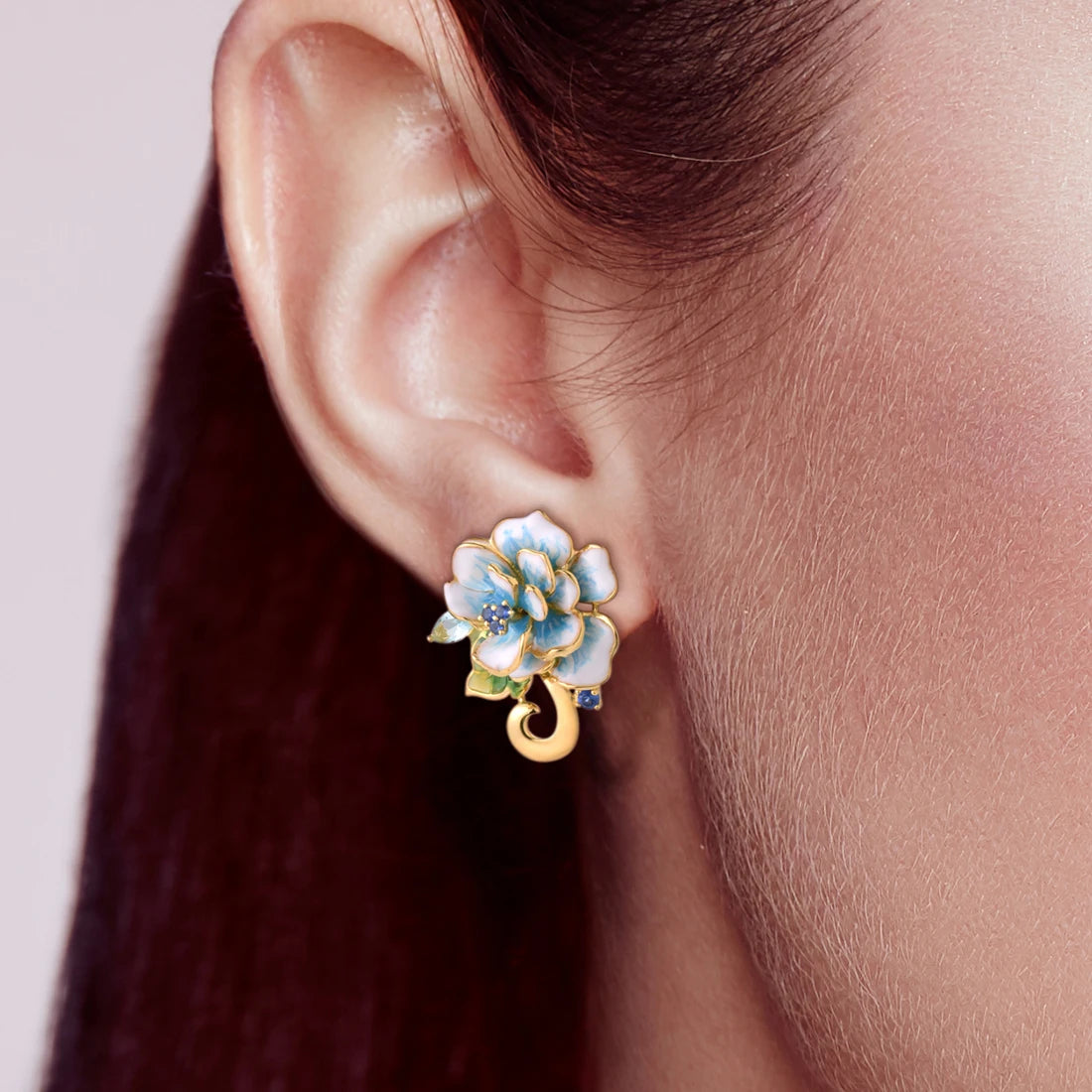 Gold-tone enamel earrings shaped like white and sky blue flowers with green leaves and sparkling stones.