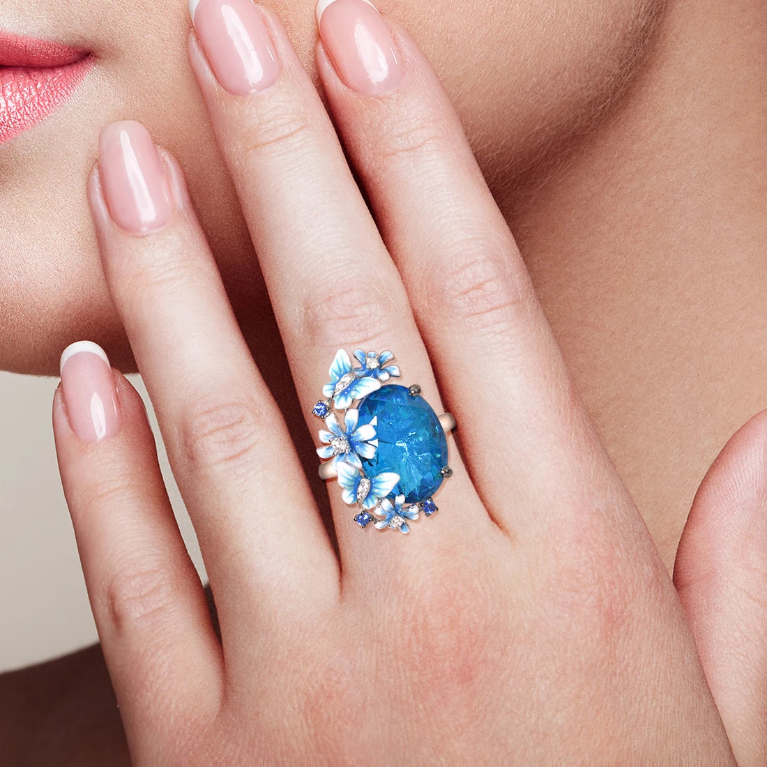 Silver ring with a large blue gemstone surrounded by butterflies and enamel flowers in soft blue tones