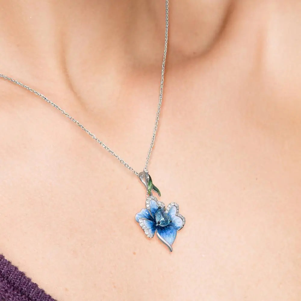 Floral silver pendant with hand-painted blue enamel petals, a teardrop-shaped aquamarine gemstone center, and a green enamel leaf accent