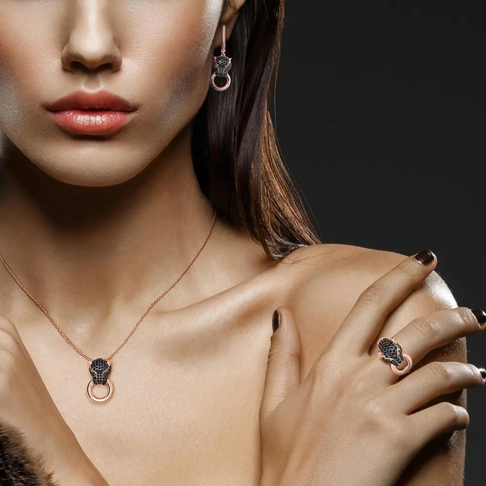 Rose gold jewelry set with panther head designs featuring black stones and green eyes, including earrings, ring, and pendant.
