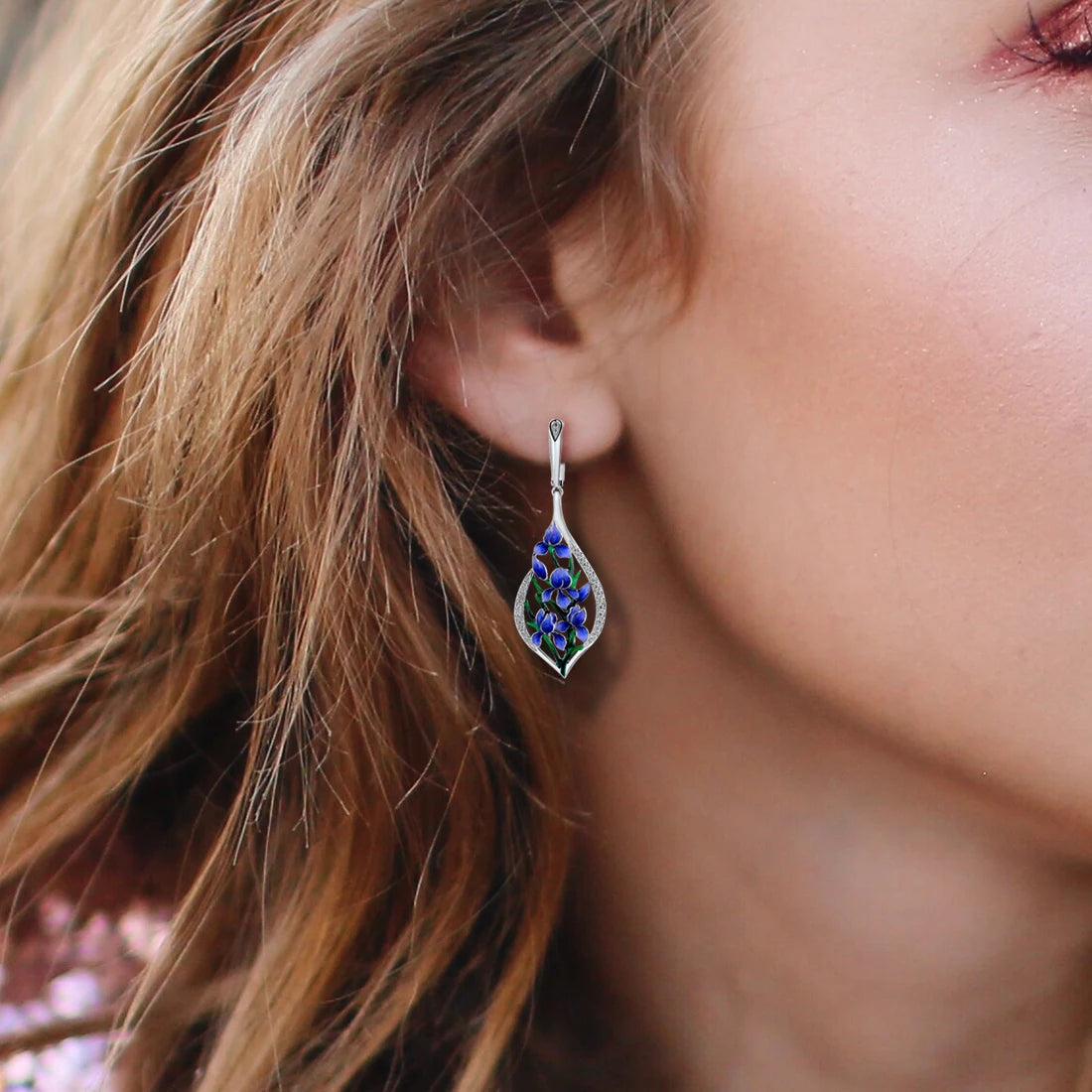 Sterling silver drop earrings featuring blue and green enamel floral vines framed in teardrop-shaped pavé-set silver
