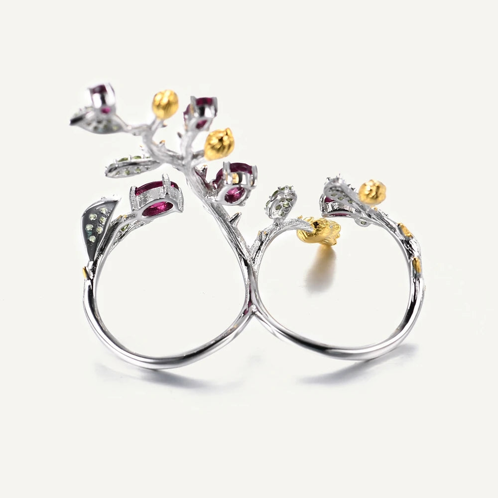 Double-finger ring with branch-like silver bands, deep pink stones, golden buds, and green pavé leaves from the Rossa Collection.