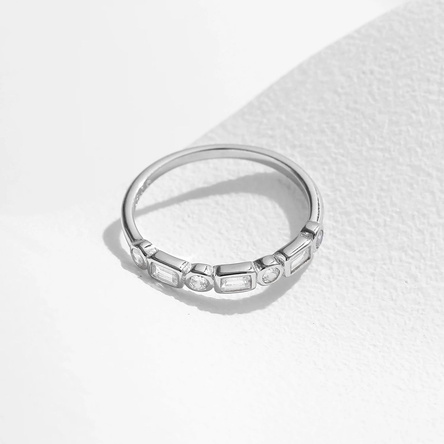 Silver ring featuring alternating round and baguette-cut white stones in a half-band setting.
