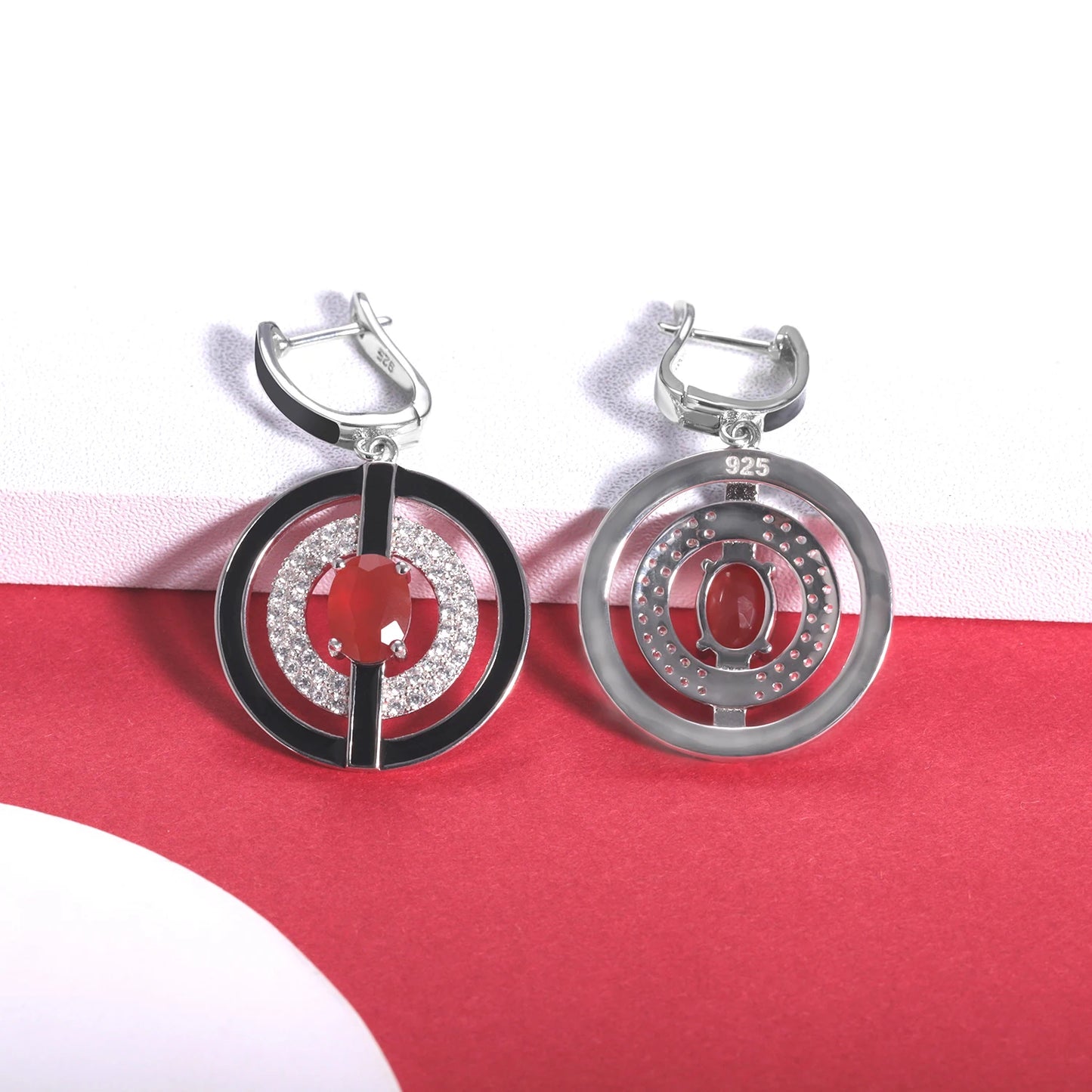 Sterling silver earrings with black enamel rings, pavé-set stones, and central red oval gems, from the Obliqua design.