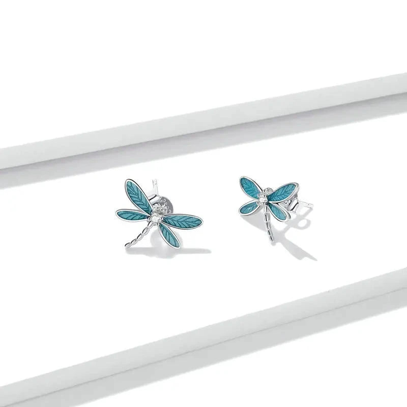 Silver dragonfly stud earrings with translucent blue enamel wings and a tiny clear gemstone on the body