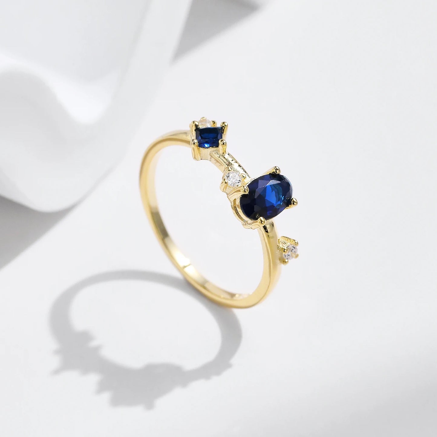 Gold-plated ring with deep blue oval and round stones set in a modern scattered design