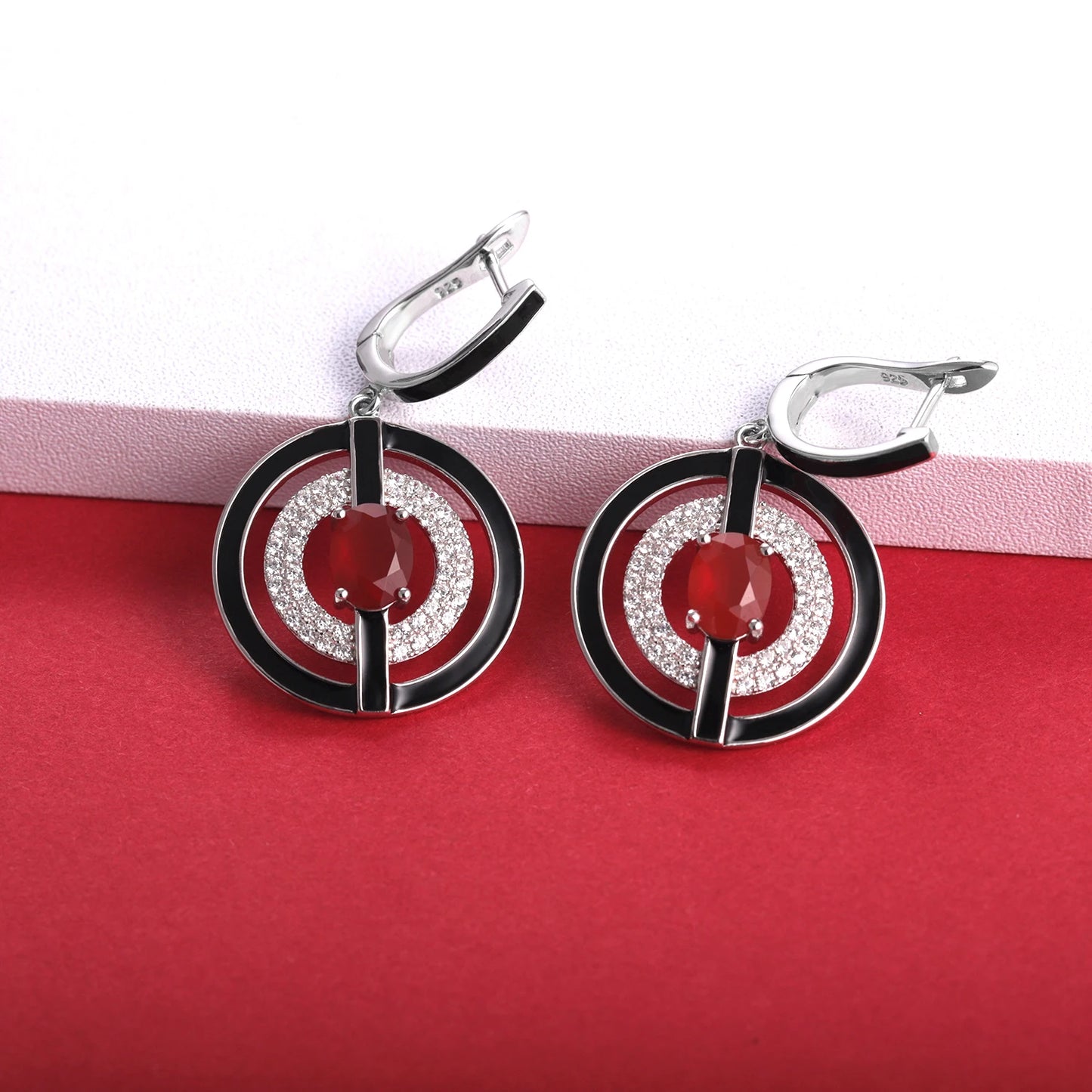Sterling silver earrings with black enamel rings, pavé-set stones, and central red oval gems, from the Obliqua design.