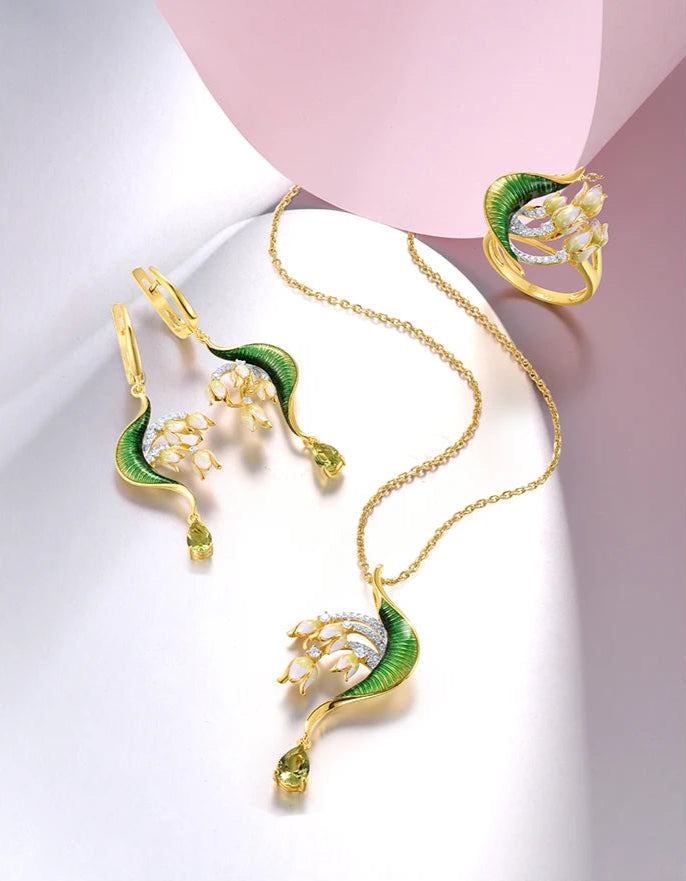 Close-up of a nature-inspired jewelry set featuring a green enameled leaf design with white and yellow floral elements, accented with sparkling stones and gold detailing.