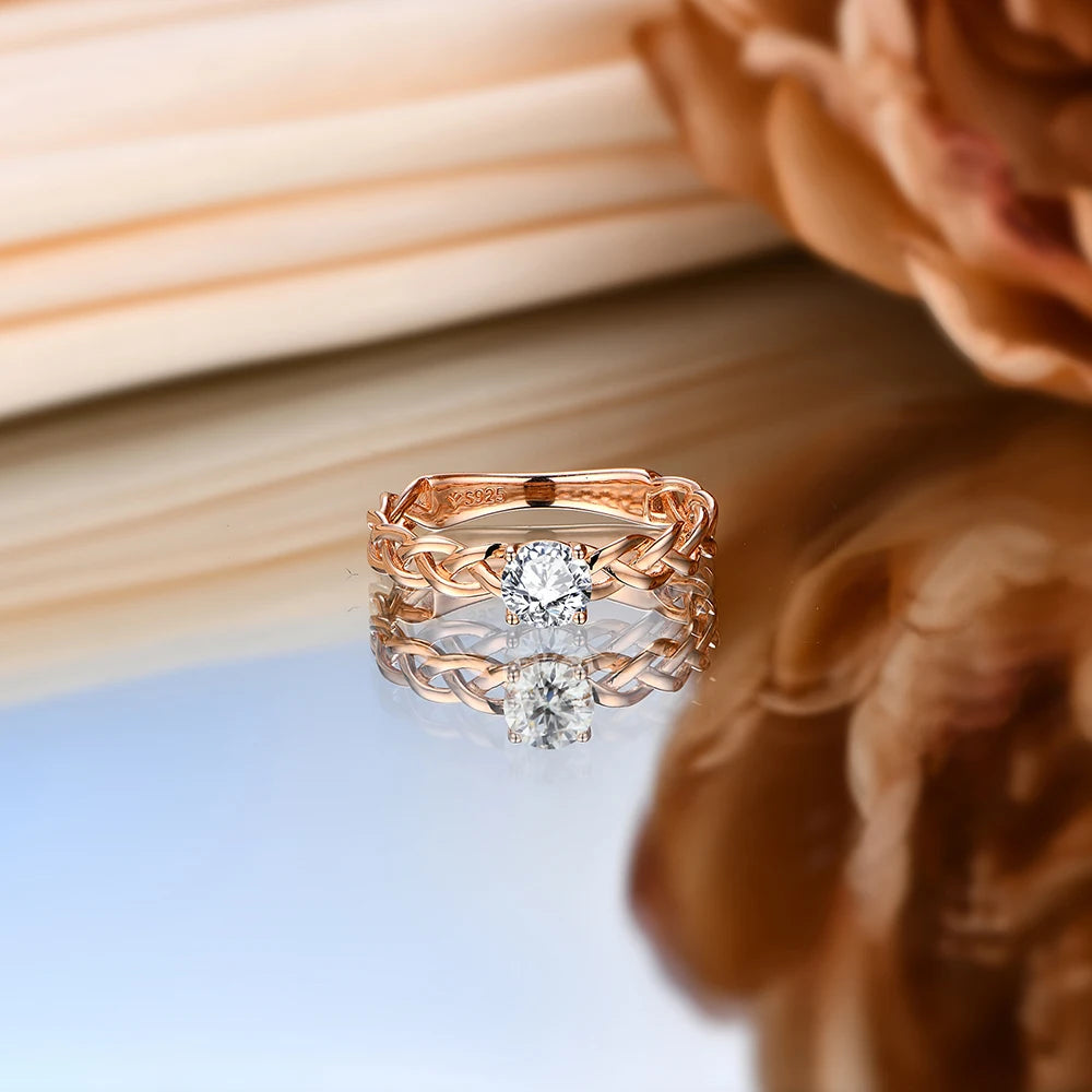 Gold ring with a braided band design and a round-cut clear central stone in a four-prong setting.