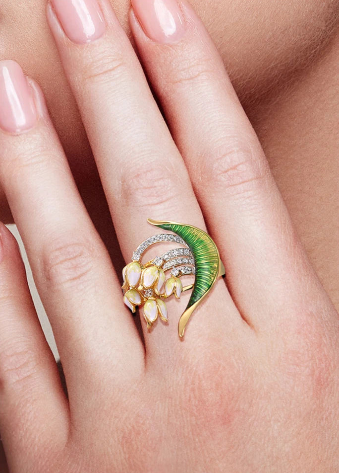 Close-up of a nature-inspired jewelry set featuring a green enameled leaf design with white and yellow floral elements, accented with sparkling stones and gold detailing.