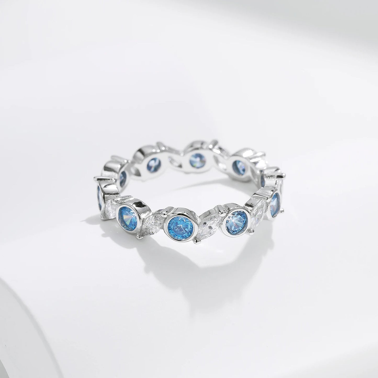 Sterling silver eternity ring with alternating light blue and clear round stones in bezel and prong settings